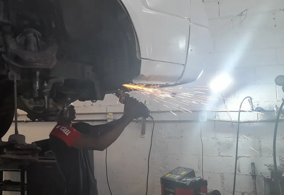 Mecânico esmerilhando a estrutura de um carro suspenso na oficina